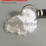 Ein Häufchen feines weißes Pulver mit der Aufschrift „Instant Leucin“ neben einem mit dem Pulver gefüllten Messlöffel aus Metall.